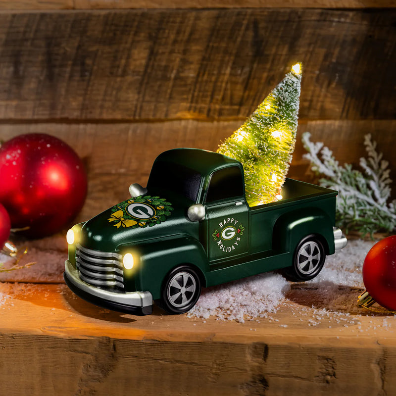 Decorative Green Bay Packers truck statue with a lit Christmas tree on a wooden surface with ornaments.