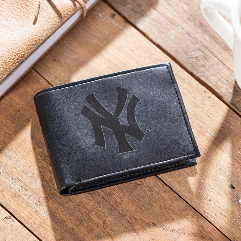 Black wallet with a New York Yankees logo on a wooden surface next to a notebook and mug.
