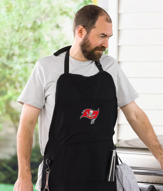 Man wearing a black apron with a Tampa Bay Buccaneers logo, standing outdoors.